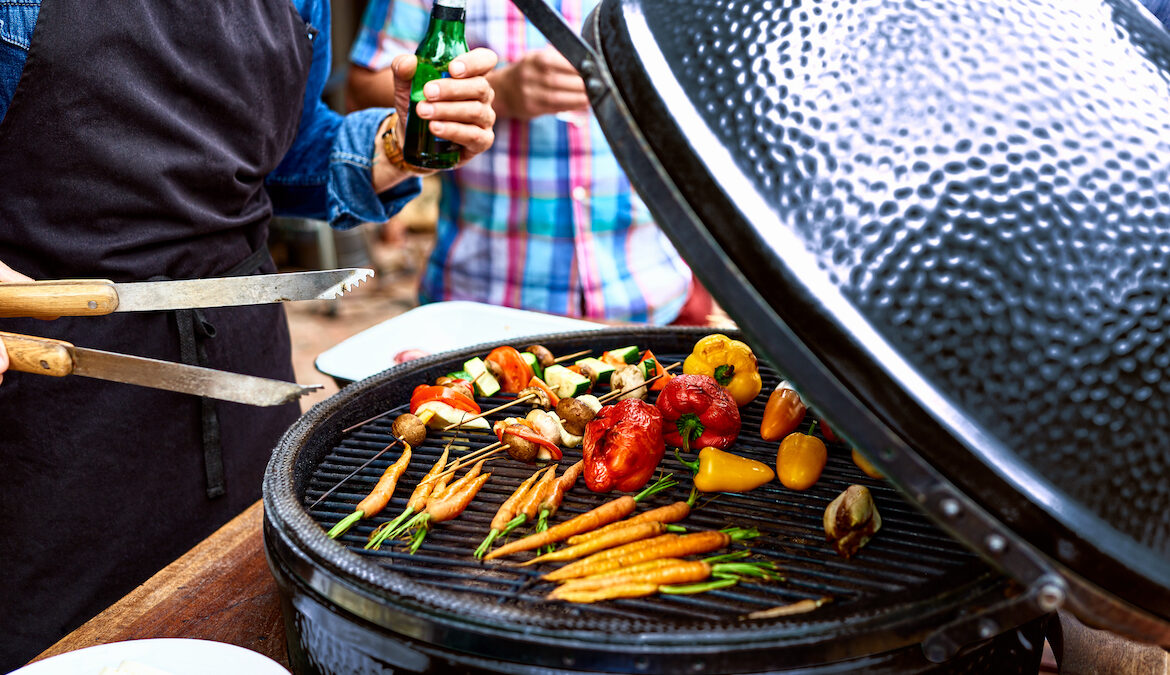 A man cooks vegetables on a grill after cleaning it with a potato.