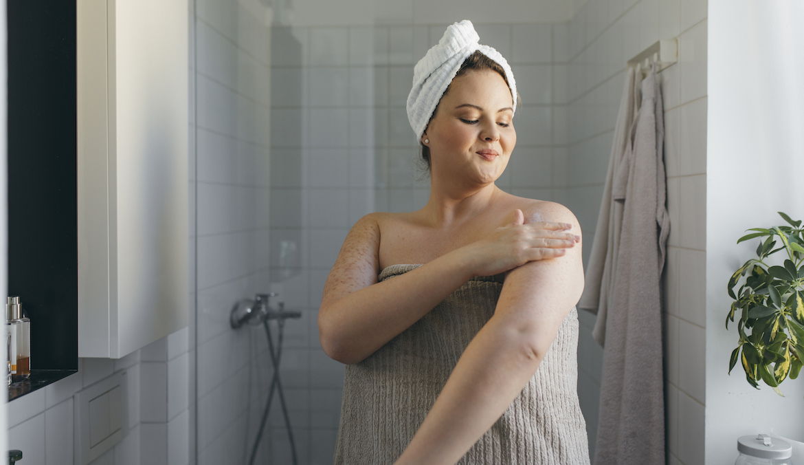 Plus size woman during a morning skin care ritual - applying body care cream onto her body.