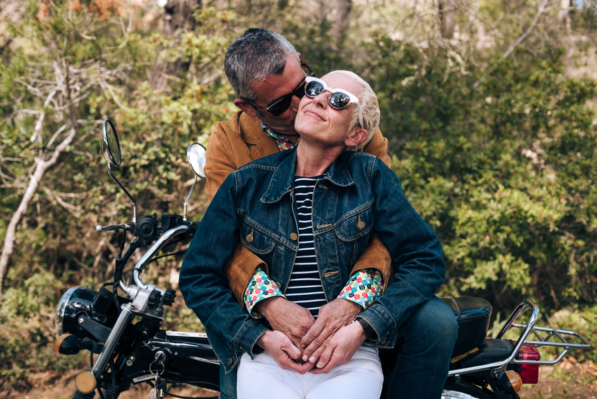 Happy middle aged couple wearing sunglasses, hugging and kissing, enjoying their lifestyle and a day outdoors.