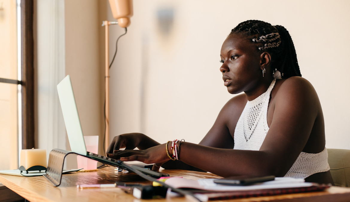 Young black woman typing on her laptop, focused on her computer while working from home sitting at her desk.