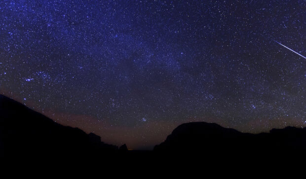 A digital image of a starry sky over The Window in Big Bend National Park, in Texas, with the streak of a single meteor in the upper left portion of the composition