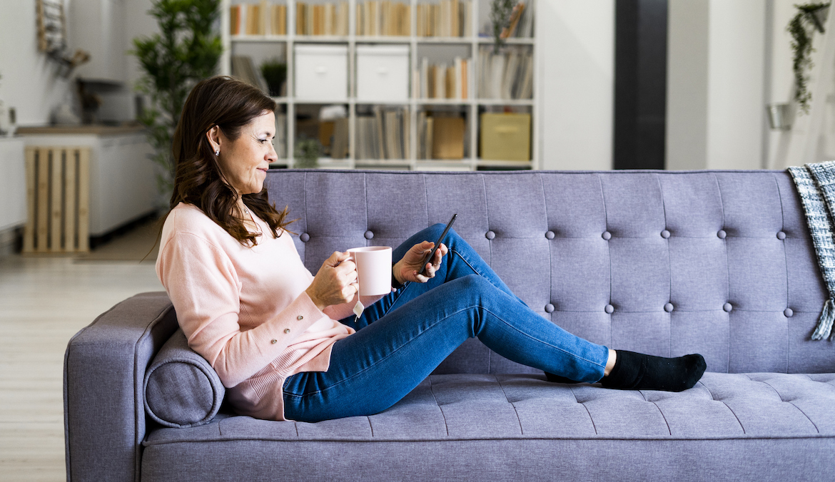 Adult woman checking smartphone drinking tea or coffee at home
