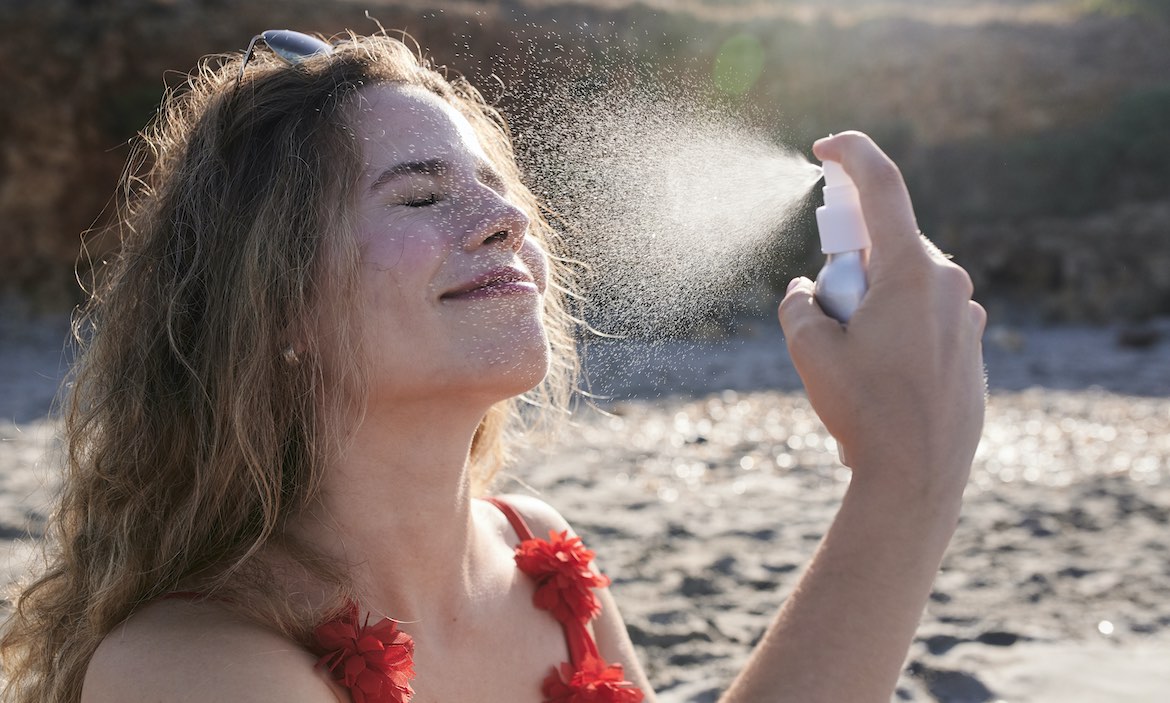 A woman applying spray sunscreen to her face.