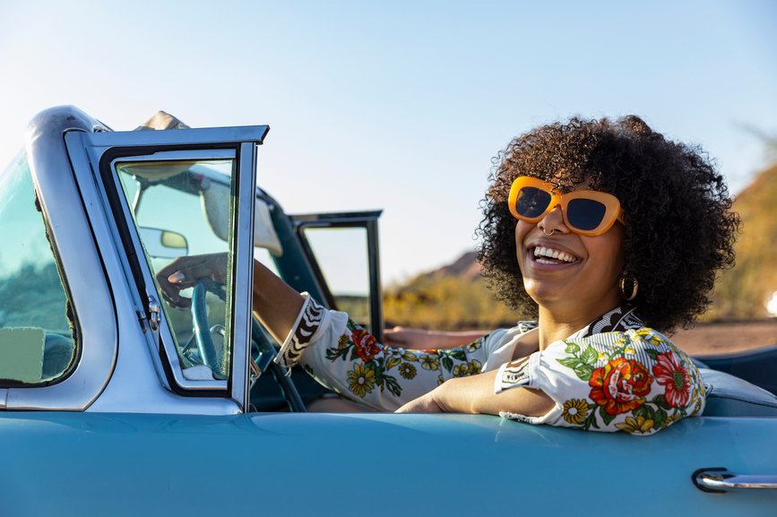 A woman wearing sunglasses drives a convertible while wearing sunscreen.