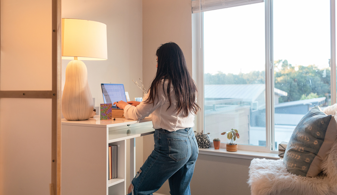 Brunette woman in her apartment using a laptop on standing desk, and working from home in the morning