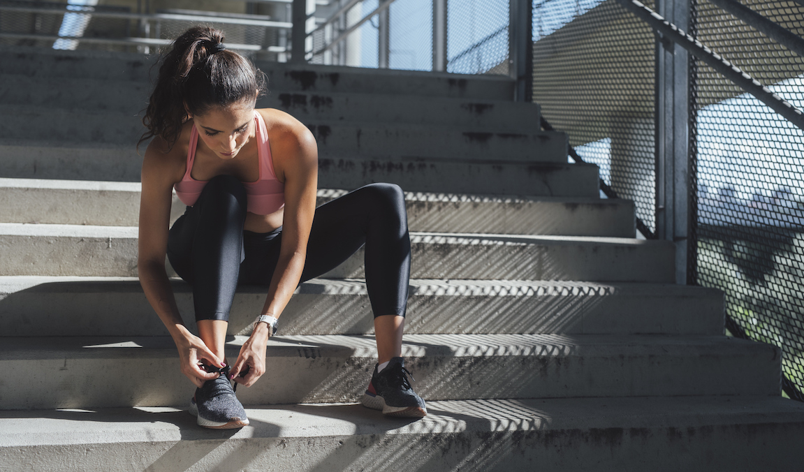 A woman ties her shoe while sitting on steps, best sneakers with arch support
