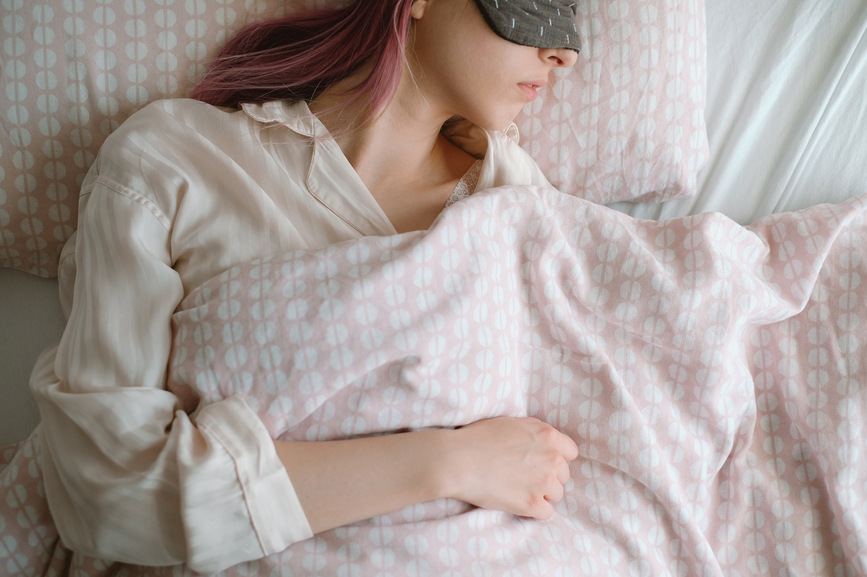 Pink hair woman sleeping in bed and wearing sleeping mask.