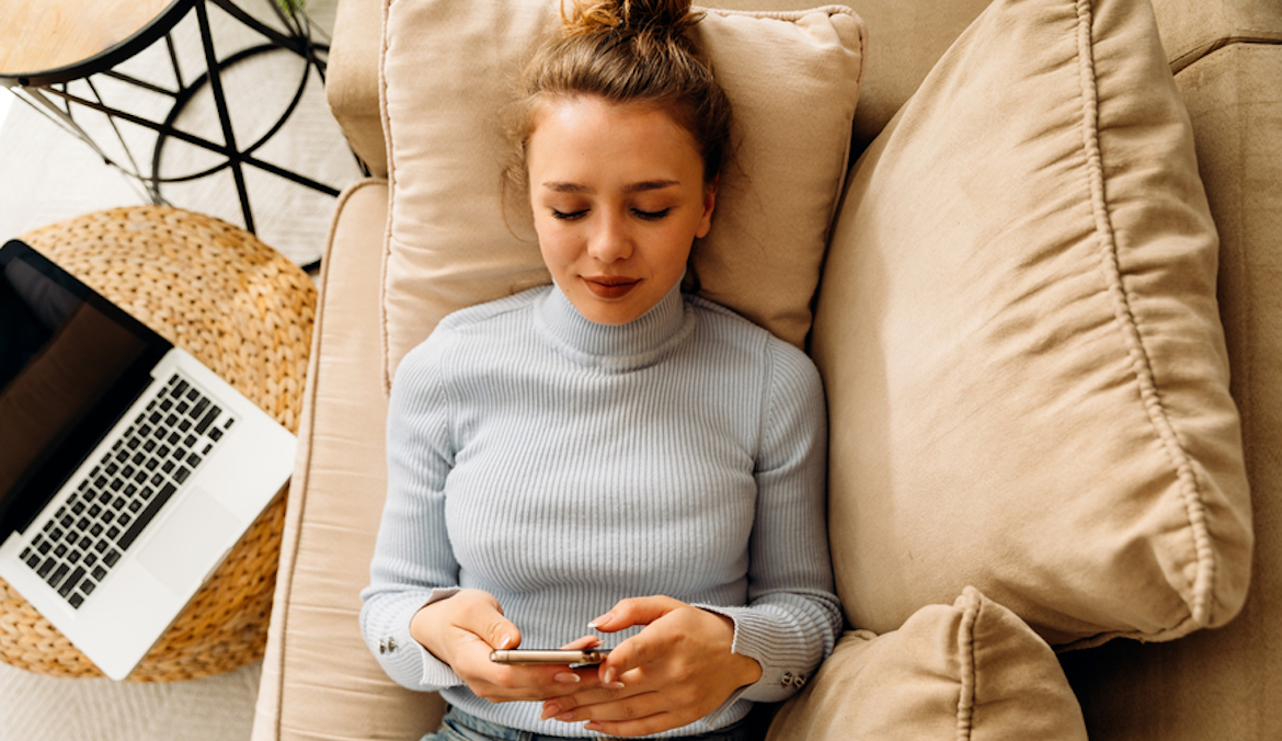 woman lying on sofa bed and texting on her mobile phone
