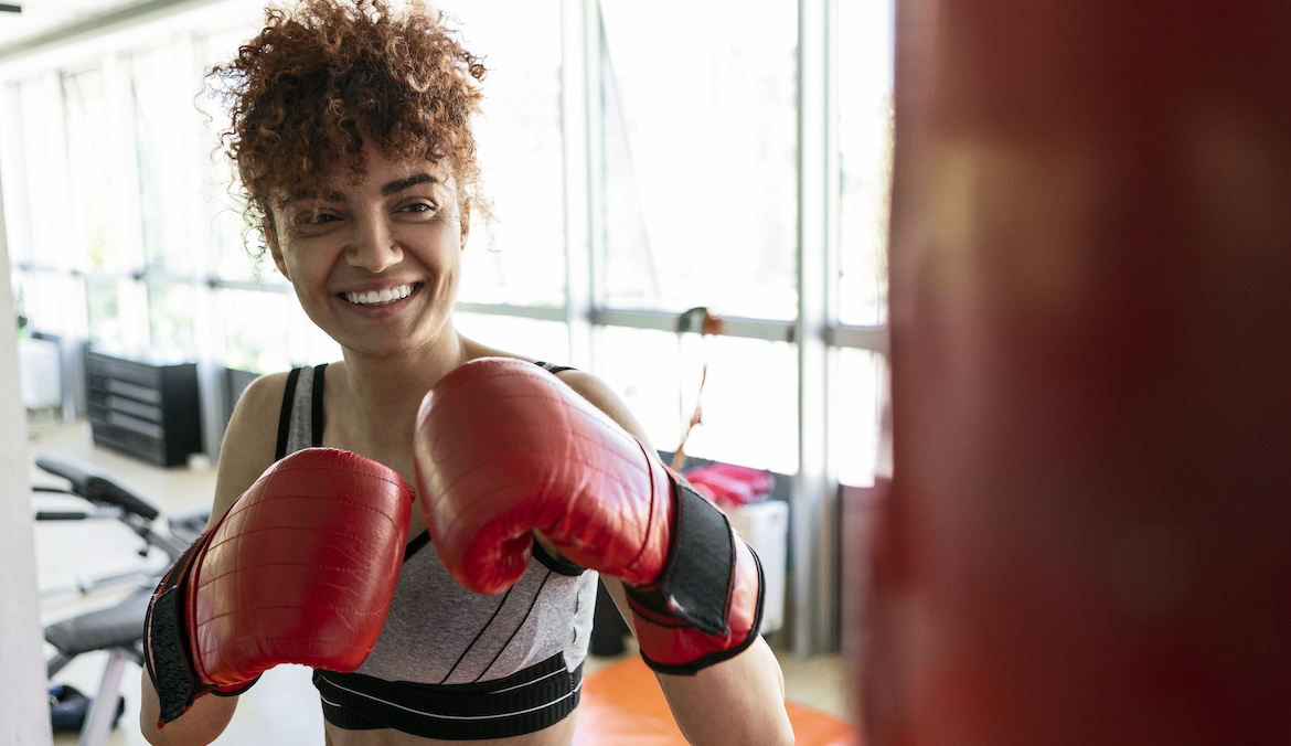 woman with boxing gloves smiling at a boxing bag