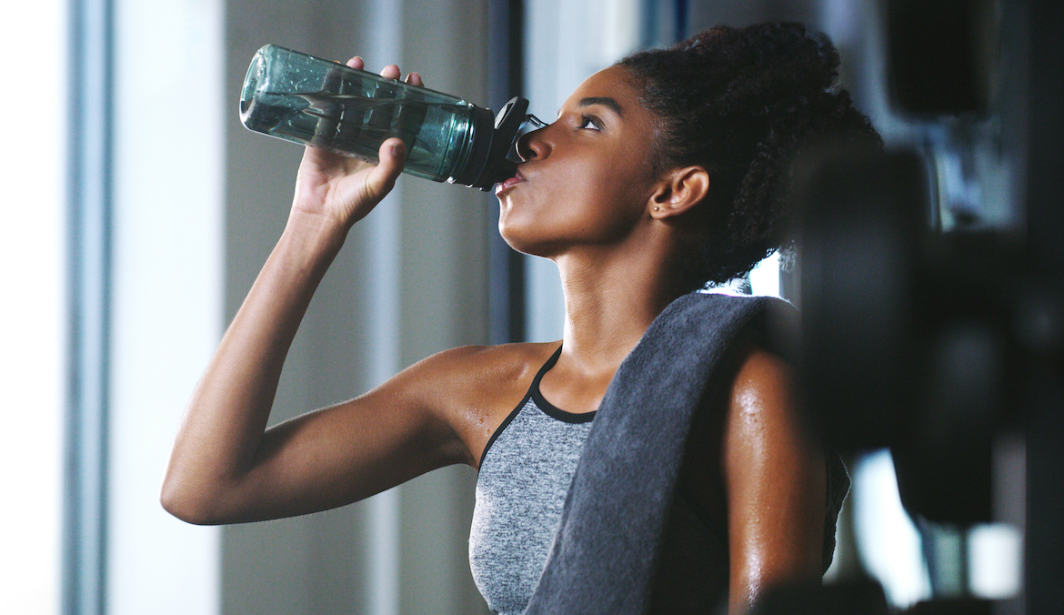 A woman drinking a pre-workout supplement at the gym