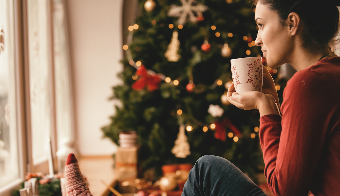 woman drinking tea sitting by christmas tree