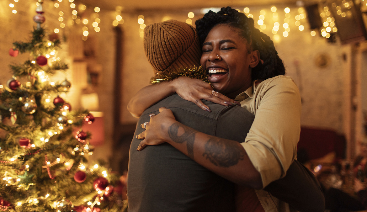 woman hugging significant other in front of a christmas tree
