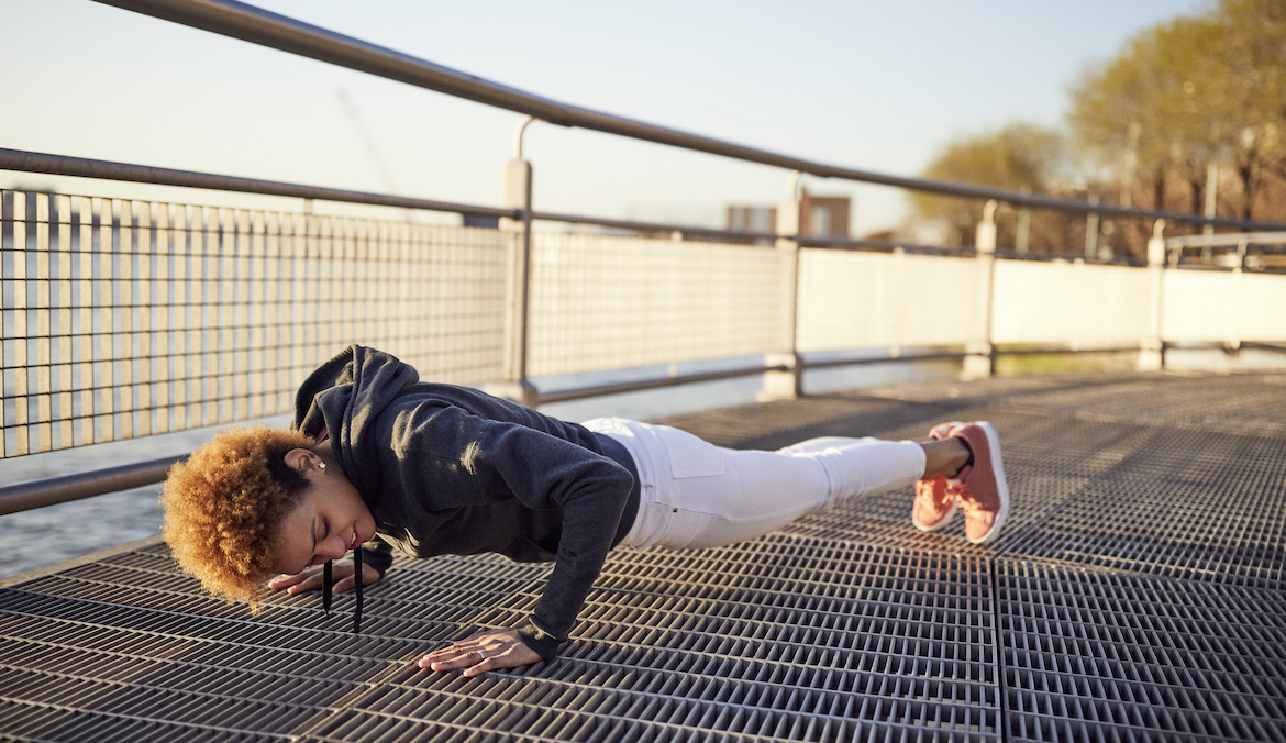 Side view of young woman doing push-ups on metallic footpath