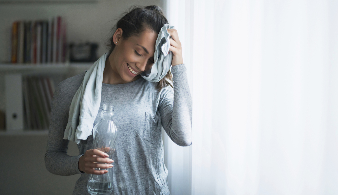 A woman wipes sweat off her forehead with a water bottle in the other hand