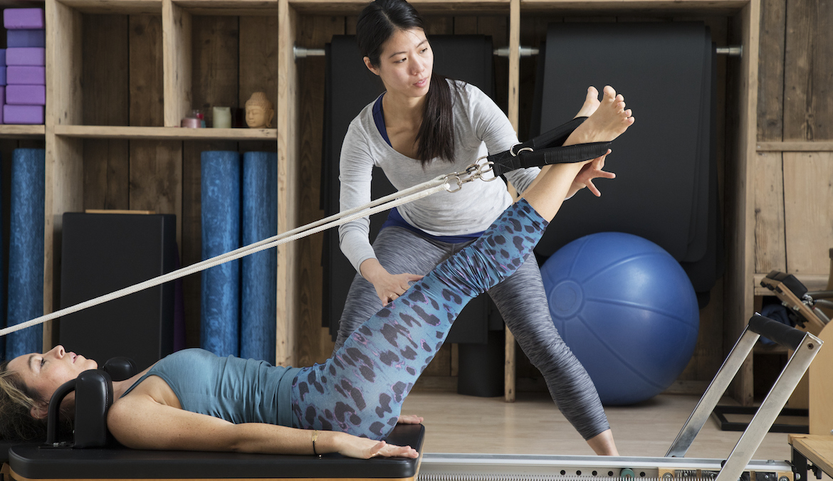 A Pilates instructor corrects a student on a reformer