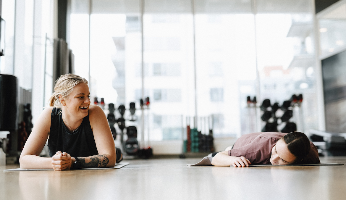 Smiling young woman looking at friend lying on mat in health club