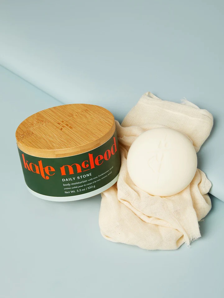 A white body lotion bar rests on the cloth next to the wooden box.