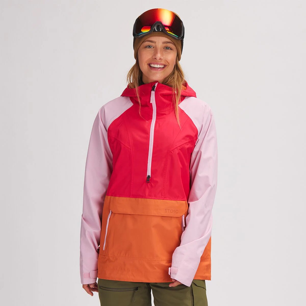 model with ski goggles wearing a stoic shell anorak in red, orange and pink which is now on sale at backcountry