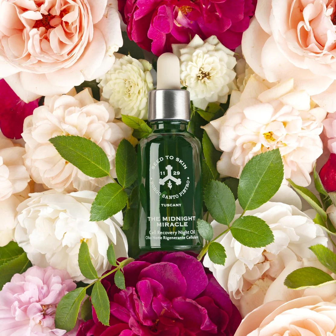 A green bottle of face oil on a bed of flowers.