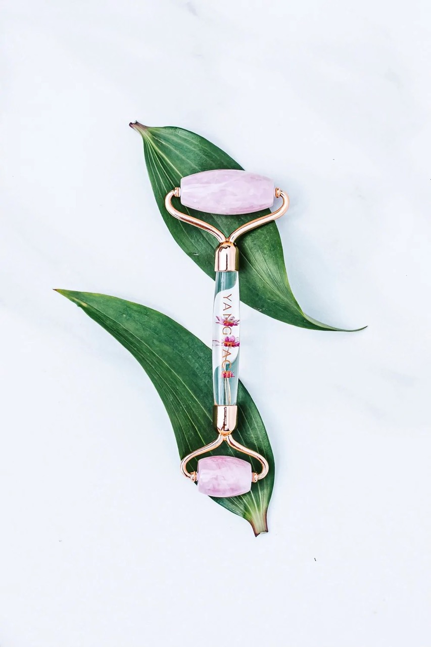 A dual-ended rose-quartz facial roller with a floral handle.