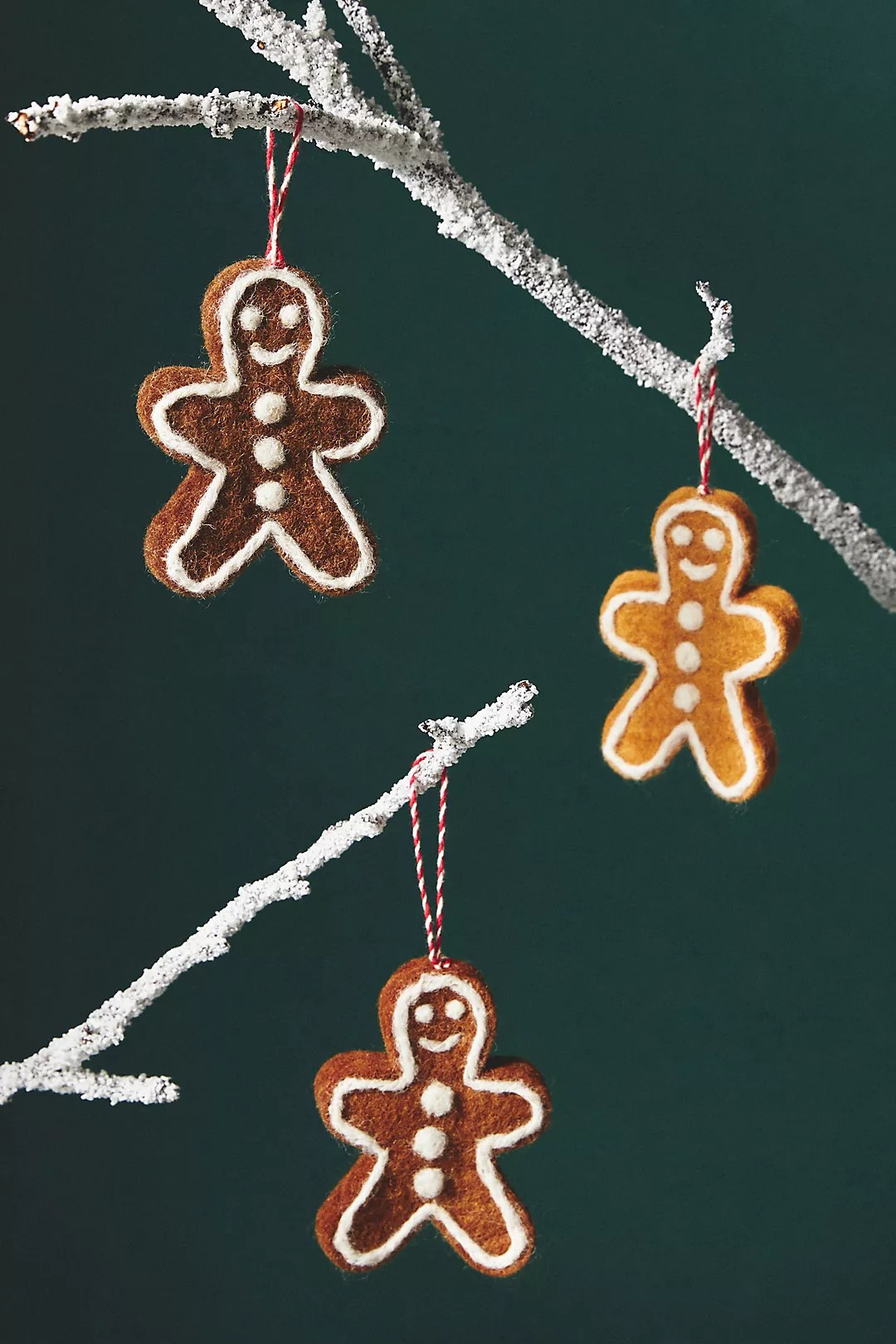Gingerbread Christmas ornaments from the anthropologie black friday sale hanging from a tree branch on a dark green background