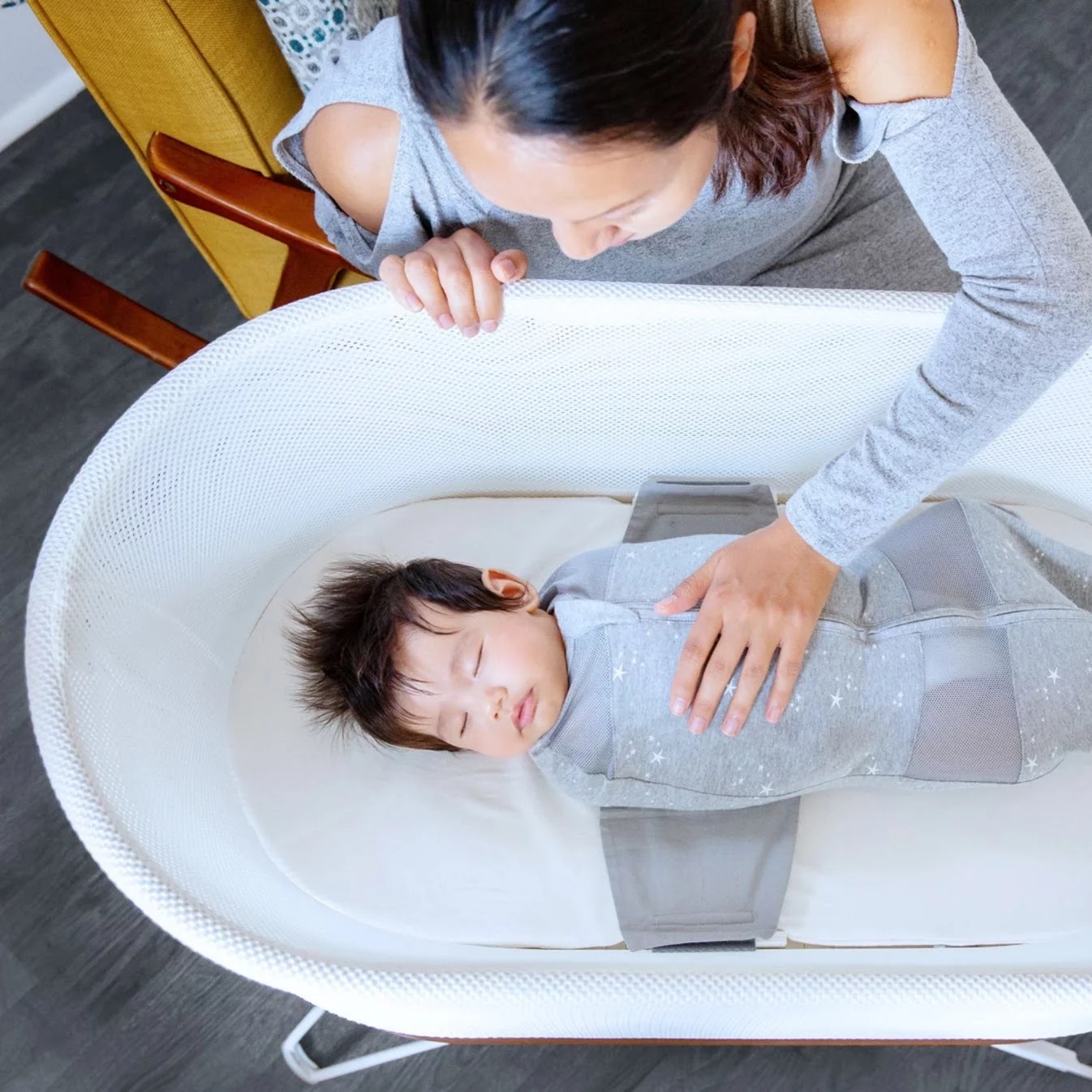 A baby in a bassinet wearing a gray swaddle.