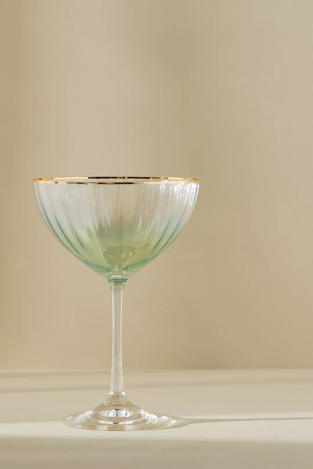 waterfall coupe glass with a gold rim and green tint on a beige background