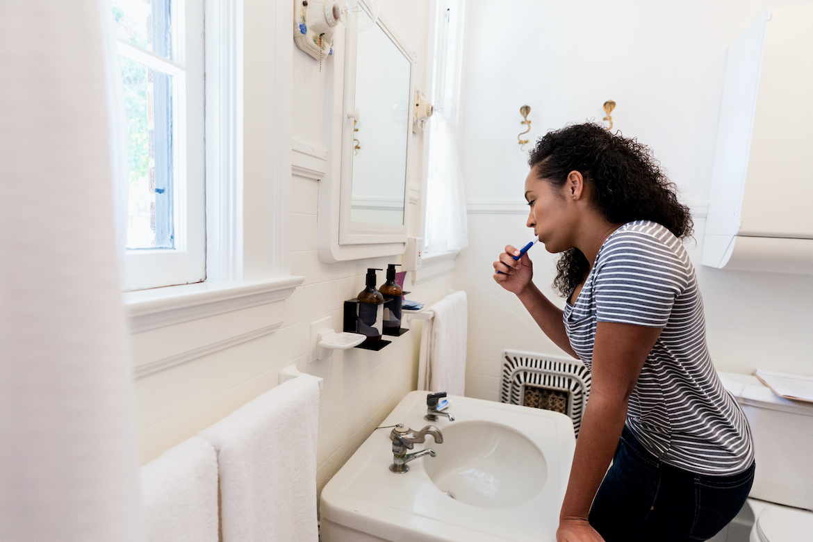 Young Black woman brushing her teeth in bathroom.