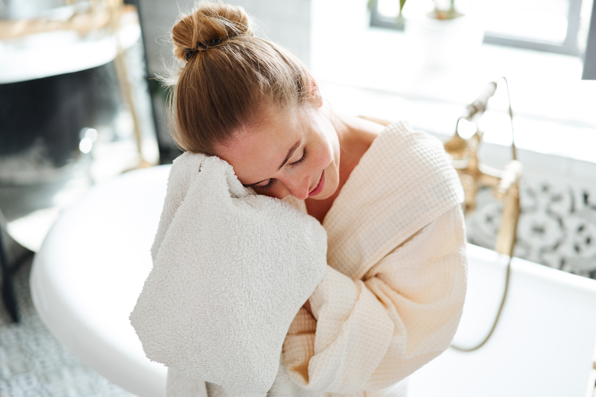A woman sitting on the edge of a bathtub dried her face with one of the best bath towels