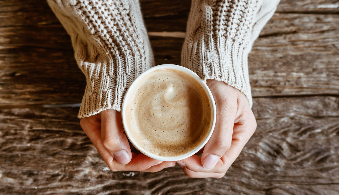 Overhead photo of a woman holding a cup of coffee in her hands while wearing a sweater.