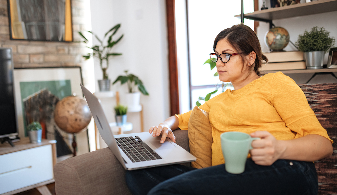 Woman working from living room, using laptop and drinking coffee