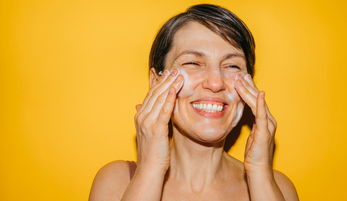A beautiful woman washing her face with facial foam in front of a yellow background