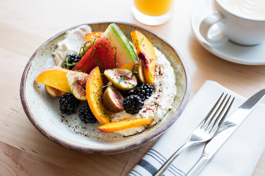 Oatmeal topped with fruit with juice and a latte for breakfast.