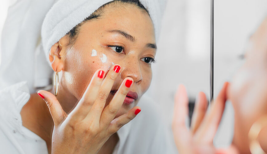 Woman wearing a bath towel applies arnica cream underneath her eyes.
