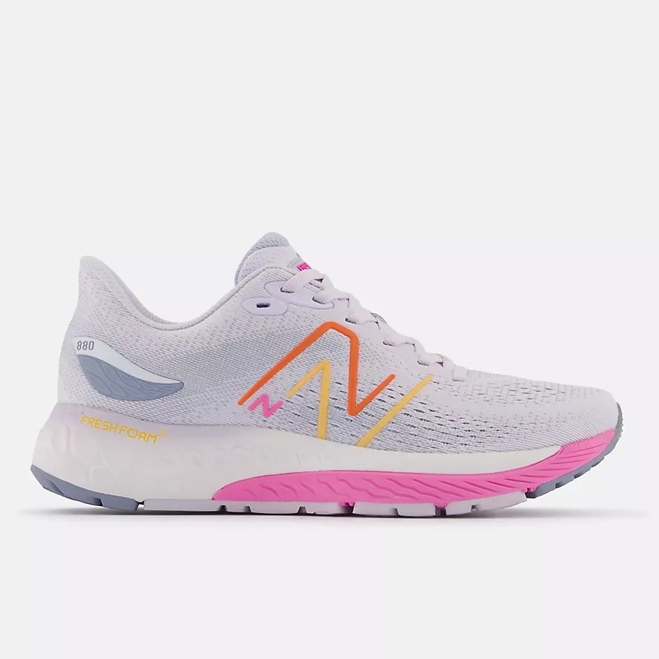 A white New Balance sneaker with pink and yellow accents viewed from the side.