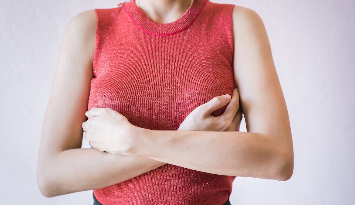 Photo of a woman crossing her arms over her chest, grasping the sides of her chest in discomfort due to nipple sensitivity syndrome.