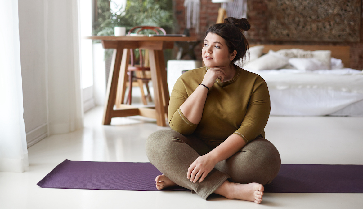 A woman sits cross-legged on a yoga mat, touching her jaw