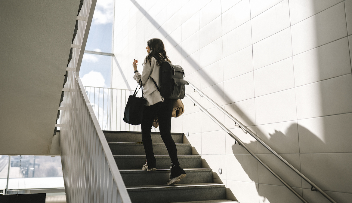 Rear view of businesswoman with backpack moving up on staircase