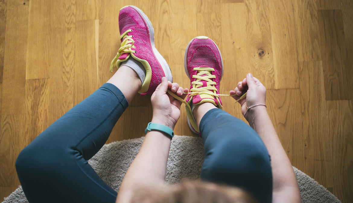 Young sporty woman with smart watch tying shoelaces