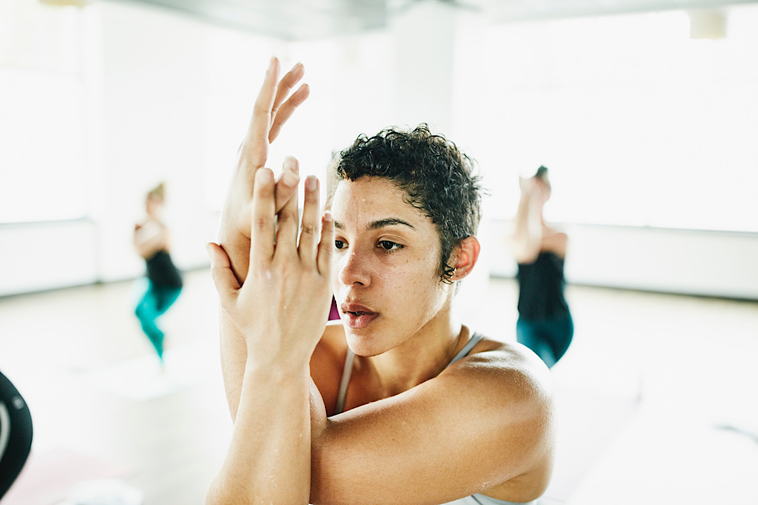 Sweating woman in eagle pose during hot yoga class in exercise studio