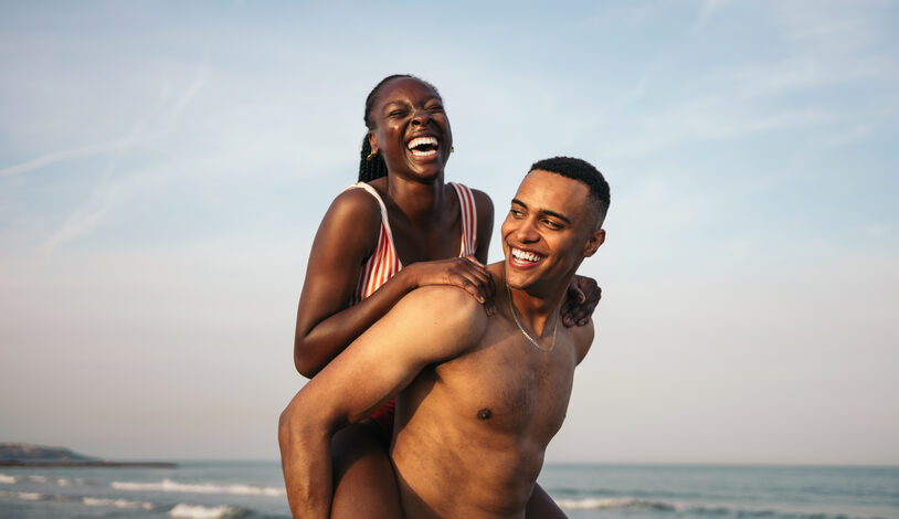 A beautiful young couple laughs while having fun on the beach.