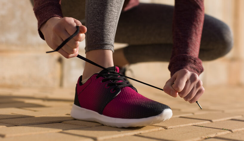 A close-up photograph of a woman in workout clothes tying the laces of her new running sneakers.