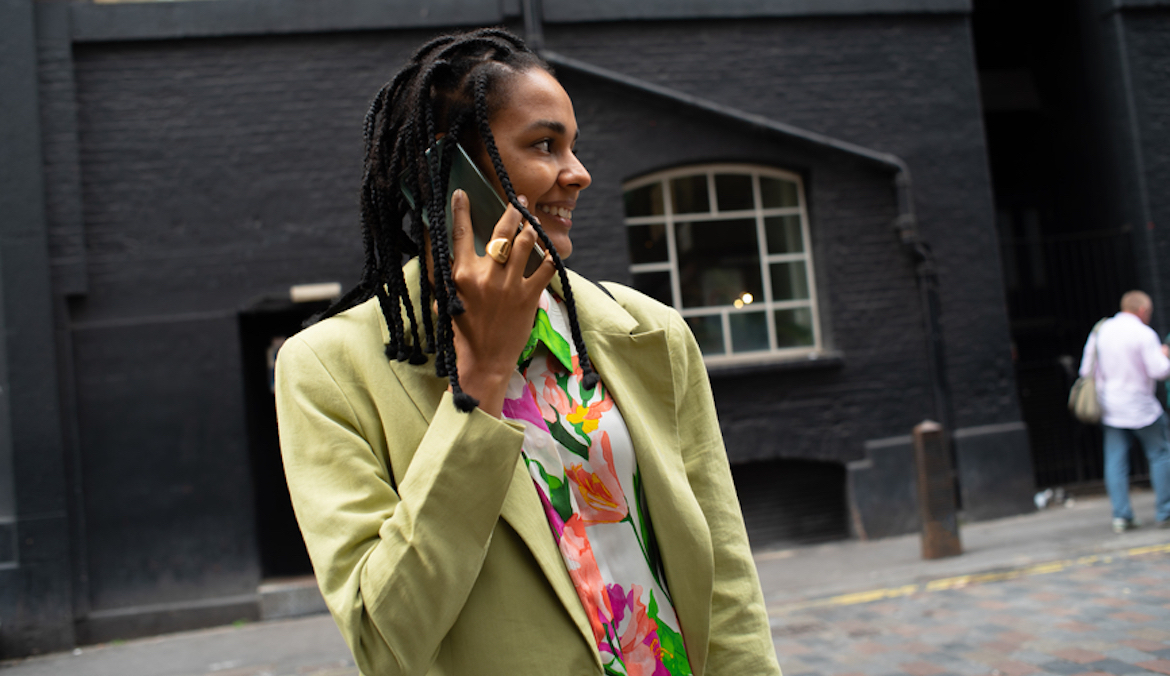 black woman on phone in a bright blazer smiling