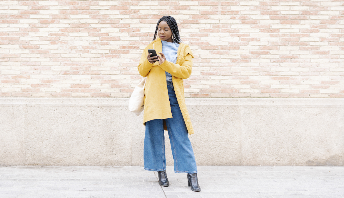 woman on her phone wearing wide leg jeans and a yellow jacket