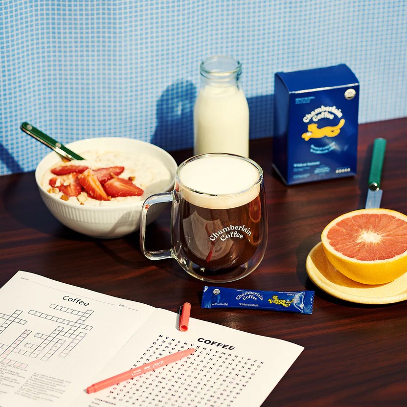 chamberlain coffee instant coffee in a mug next to a crossword, fruit and bowl of yogurt