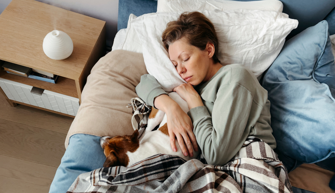 woman in bed with dog feeling sick due to covid immunity debt