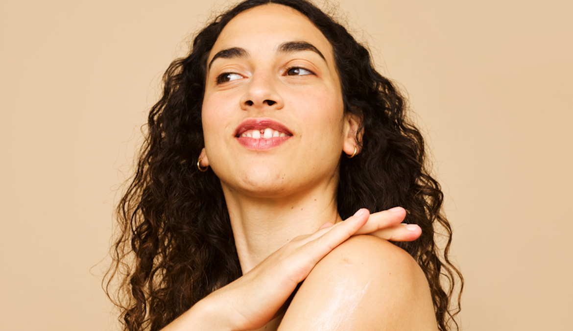 woman with curly hair applying humanrace body cream to her shoulders
