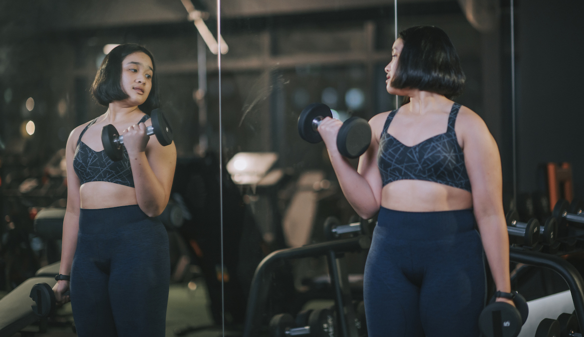 A woman lifting weights looks in a mirror.