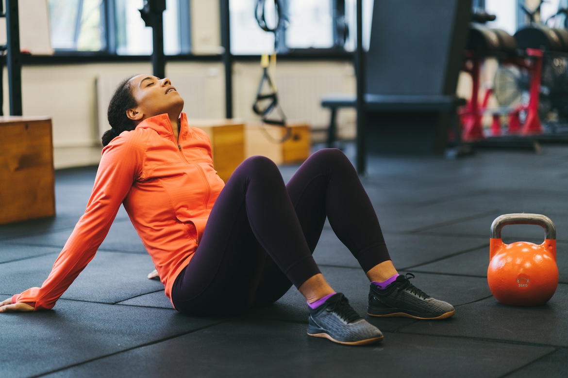 Person wearing orange shirt and black leggings in gym tired after workout