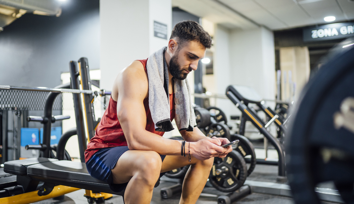 Man in gym rests on the bench using his phone